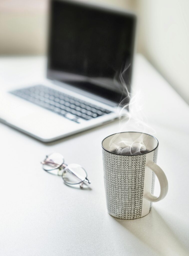 Steaming coffee on a desk next to a laptop and glasses. Perfect for productivity themes.